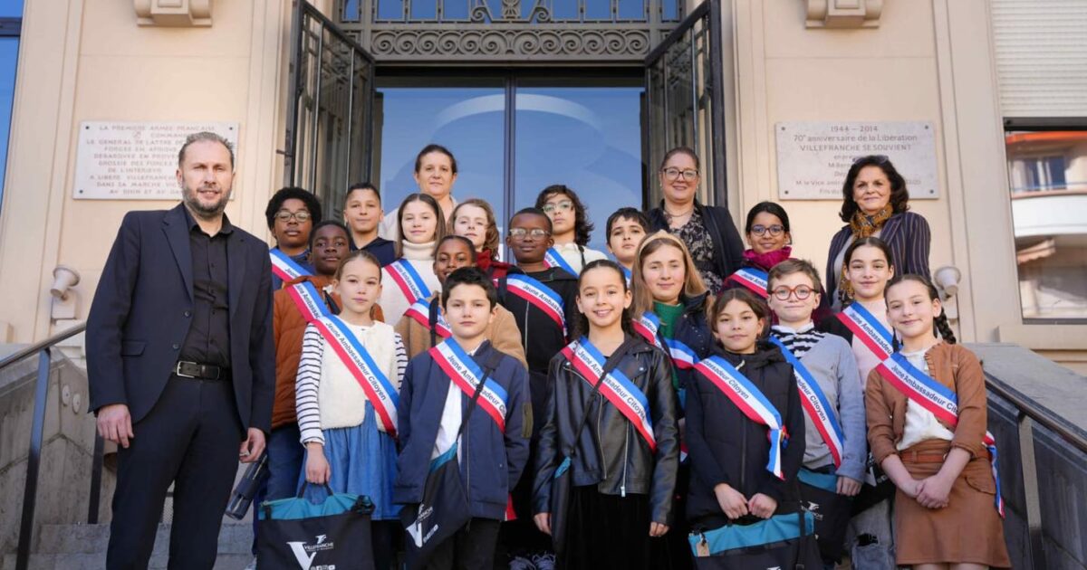 Photo d'enfants arborant la bannière des jeunes ambassadeurs citoyen accompagné du maire devant l'hôtel de ville