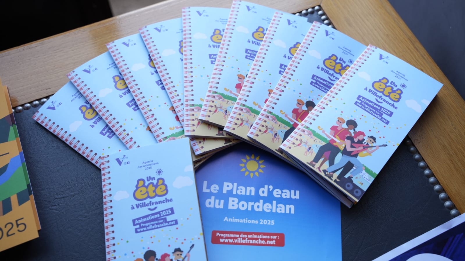 Photo illustrant les supports papiers lors de la conférence de presse pour Un été à Villefranche. Des livrets pour connaître toutes les animations durant l'été et la plaquette spécifique au Plan d'eau du Bordelan