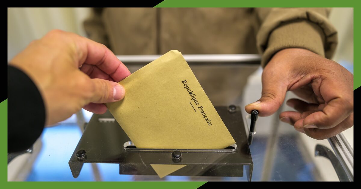 Photo illustrant une main qui dépose une enveloppe de vote de couleur kraft / marron dans une urne.